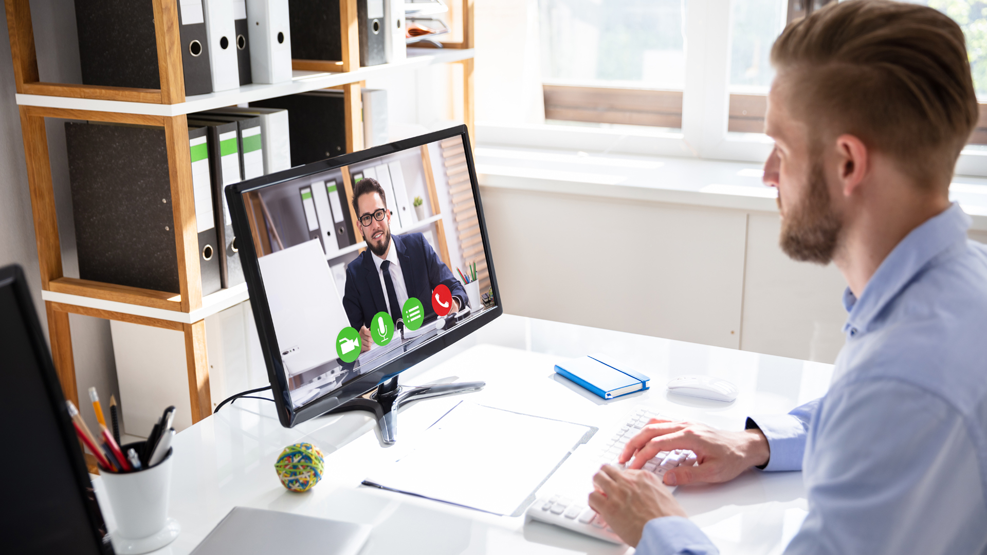 Business man in his office looking at his computer monitor with a client smiling back on virtual conference call